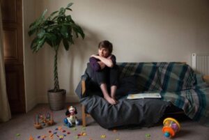 Photograph of woman looking sad with toys scattered across floor.